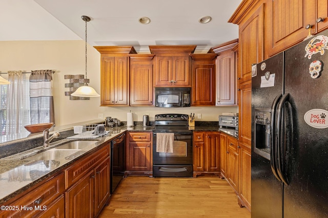 kitchen featuring black appliances, dark stone counters, light wood finished floors, a sink, and hanging light fixtures