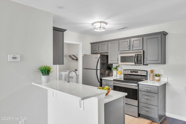 kitchen featuring appliances with stainless steel finishes, gray cabinets, a peninsula, light countertops, and a kitchen breakfast bar