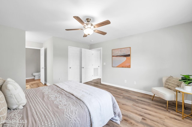 bedroom featuring baseboards, wood finished floors, ensuite bathroom, and ceiling fan