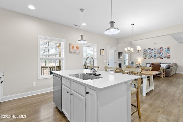 kitchen featuring baseboards, dishwasher, a sink, open floor plan, and light wood-style flooring