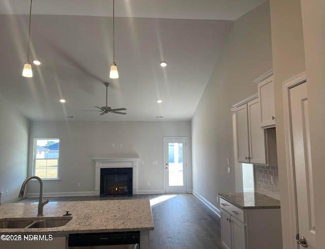 kitchen with a fireplace with flush hearth, light stone counters, dishwasher, a sink, and baseboards
