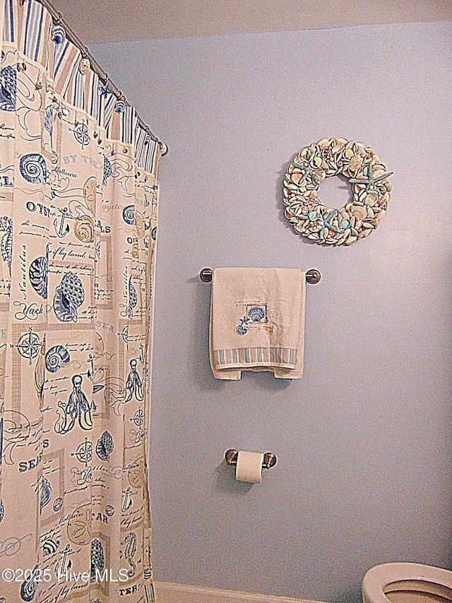 full bath featuring toilet, a shower with curtain, and baseboards
