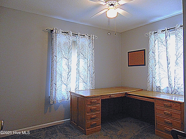 unfurnished office with dark carpet, built in desk, and ceiling fan