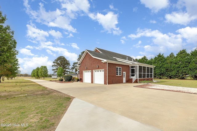 view of property exterior with a garage, a sunroom, a yard, brick siding, and driveway