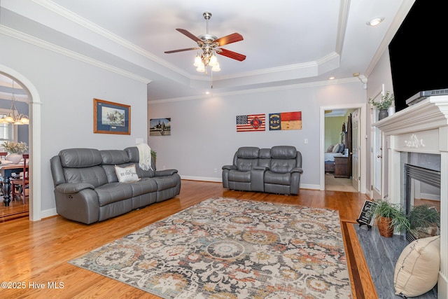 living room featuring a raised ceiling, a high end fireplace, crown molding, wood finished floors, and ceiling fan with notable chandelier