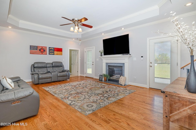 living area featuring crown molding, wood finished floors, a ceiling fan, and a raised ceiling