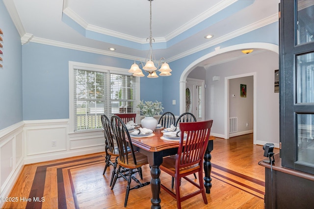 dining area featuring a tray ceiling, arched walkways, light wood-style flooring, visible vents, and a chandelier