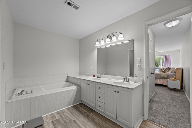 bathroom featuring visible vents, double vanity, wood finished floors, connected bathroom, and a sink