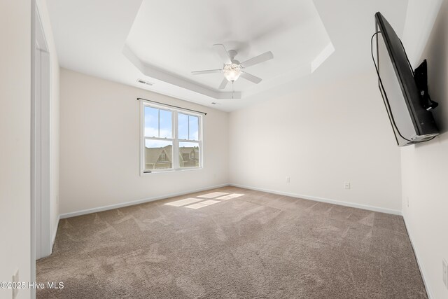 carpeted empty room featuring visible vents, baseboards, a ceiling fan, and a raised ceiling