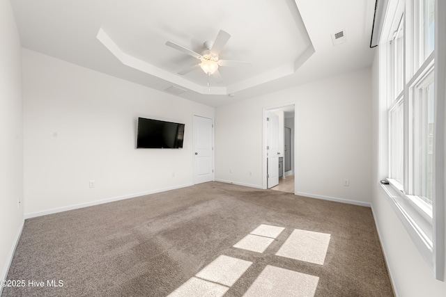unfurnished bedroom with a ceiling fan, visible vents, carpet flooring, a raised ceiling, and baseboards