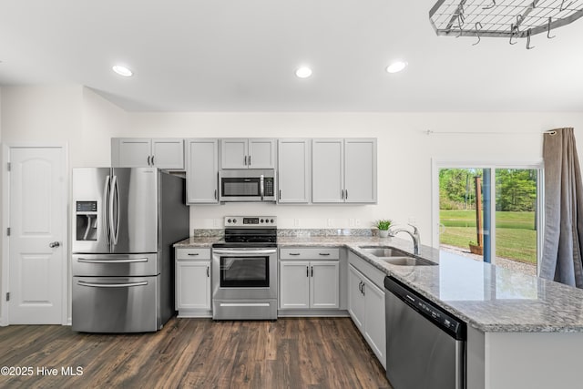 kitchen featuring dark wood finished floors, light stone countertops, a peninsula, appliances with stainless steel finishes, and a sink