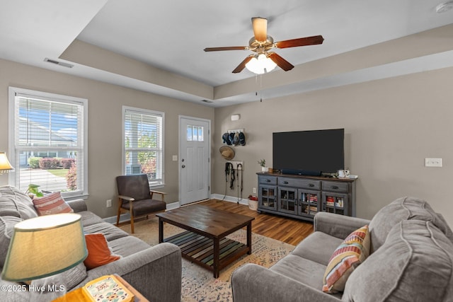 living room with a tray ceiling, baseboards, visible vents, ceiling fan, and wood finished floors