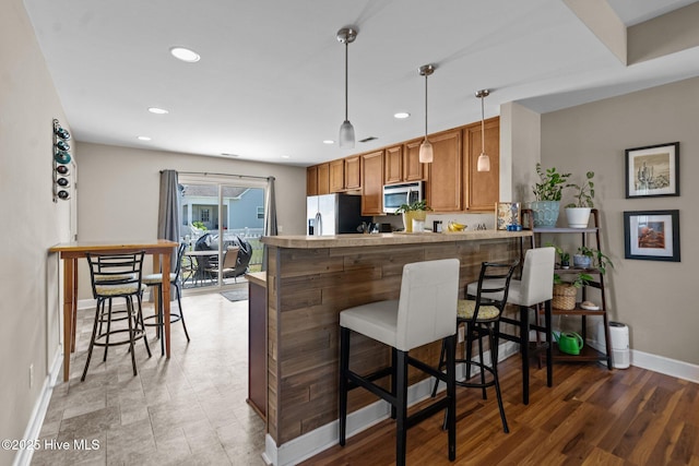 kitchen featuring baseboards, brown cabinetry, stainless steel microwave, a peninsula, and fridge with ice dispenser