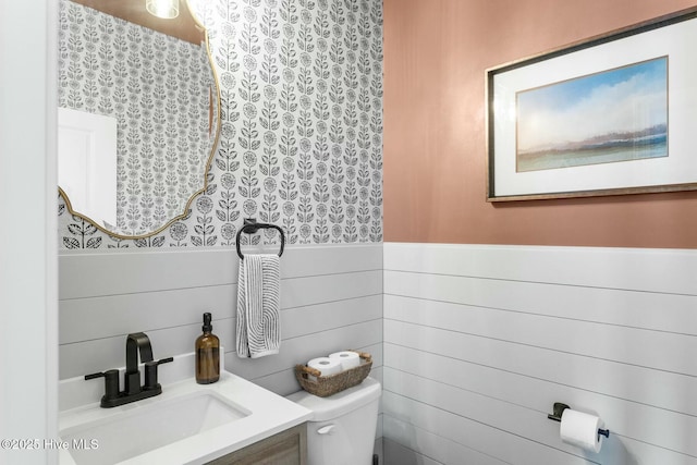 half bathroom with toilet, vanity, and a wainscoted wall