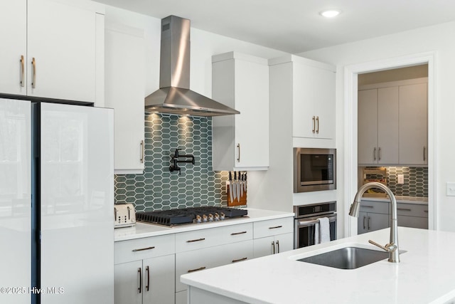 kitchen with appliances with stainless steel finishes, wall chimney range hood, recessed lighting, decorative backsplash, and a sink