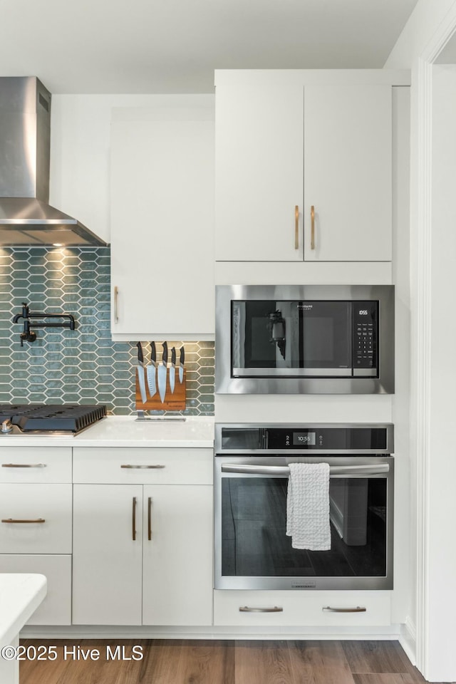 kitchen featuring wall chimney exhaust hood, gas stovetop, light countertops, oven, and built in microwave