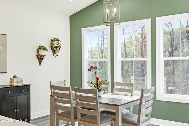 dining area featuring a chandelier, wood finished floors, baseboards, and lofted ceiling