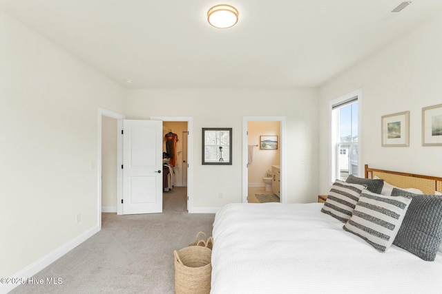 carpeted bedroom featuring a spacious closet, visible vents, baseboards, and connected bathroom