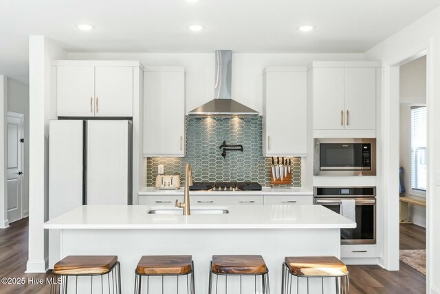 kitchen with dark wood-style flooring, light countertops, wall chimney exhaust hood, a breakfast bar area, and stainless steel appliances