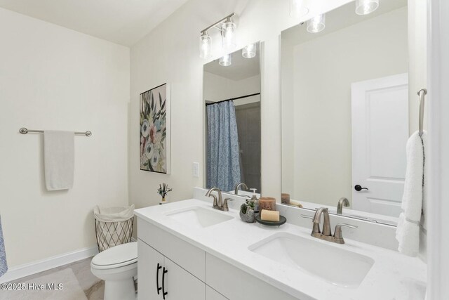 full bath with double vanity, baseboards, a sink, and toilet