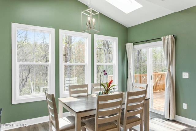 dining room featuring a chandelier, a skylight, wood finished floors, and baseboards