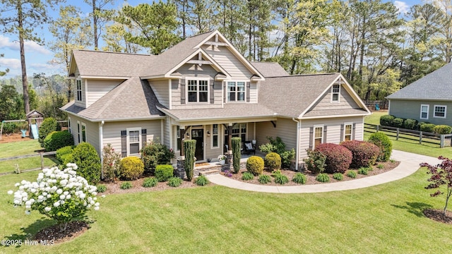 craftsman house featuring a shingled roof, covered porch, a front yard, and fence