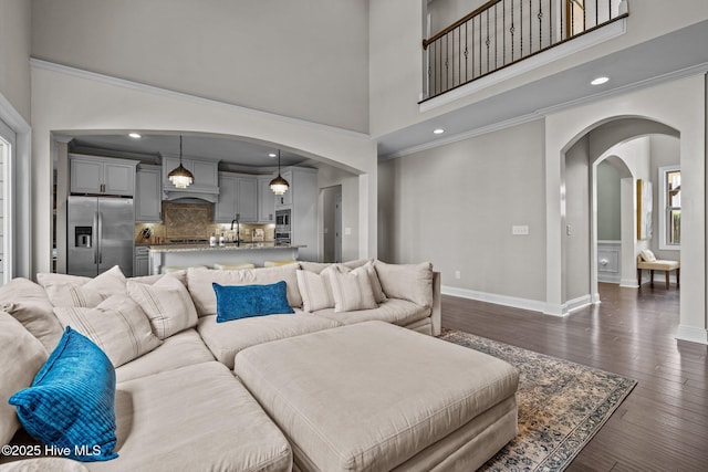 living area featuring dark wood-type flooring, arched walkways, a high ceiling, and baseboards