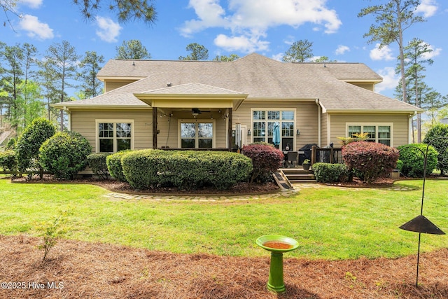 back of property with roof with shingles, a ceiling fan, and a lawn