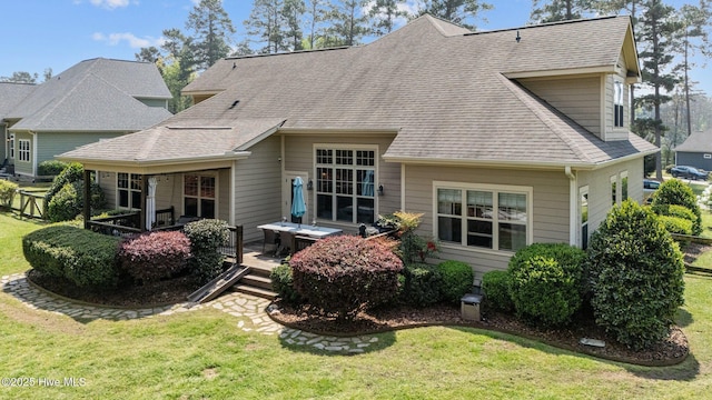 rear view of house with a shingled roof, a wooden deck, and a lawn