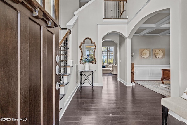 entrance foyer with arched walkways, dark wood finished floors, beam ceiling, stairway, and coffered ceiling