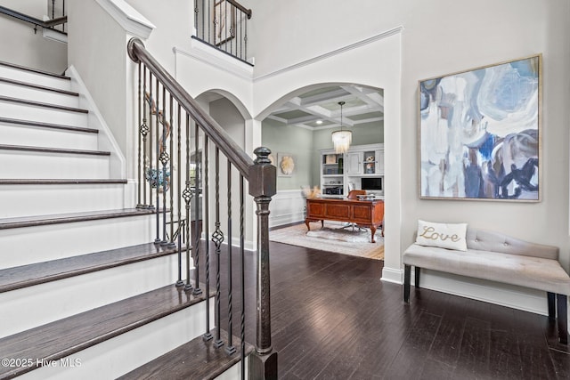 staircase featuring beamed ceiling, arched walkways, hardwood / wood-style floors, and coffered ceiling