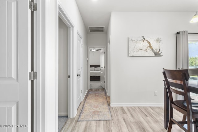 corridor with light wood-style floors, visible vents, and baseboards