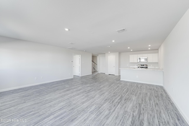 unfurnished living room with light wood-type flooring, baseboards, recessed lighting, stairs, and visible vents