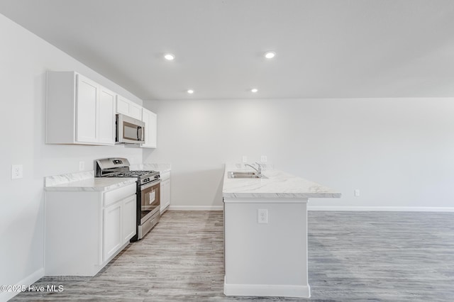 kitchen with baseboards, white cabinets, a sink, light wood finished floors, and stainless steel appliances