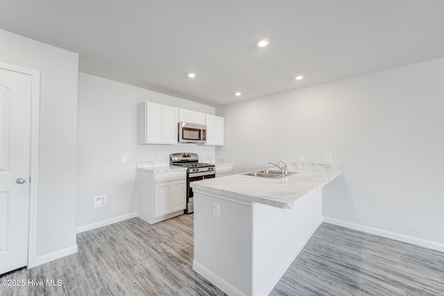 kitchen featuring white cabinets, a sink, stainless steel appliances, light wood finished floors, and baseboards