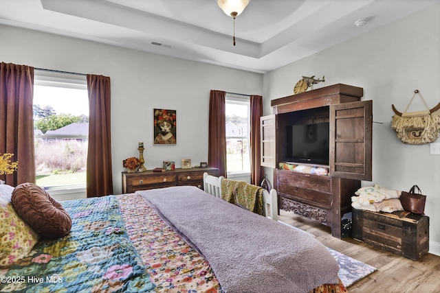 bedroom with a tray ceiling, wood finished floors, visible vents, and multiple windows