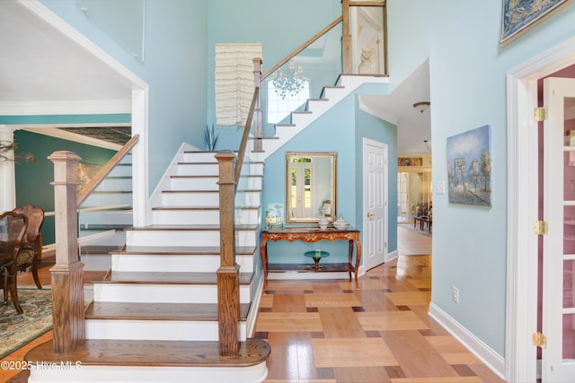 stairway with baseboards, ornamental molding, a high ceiling, and wood finished floors