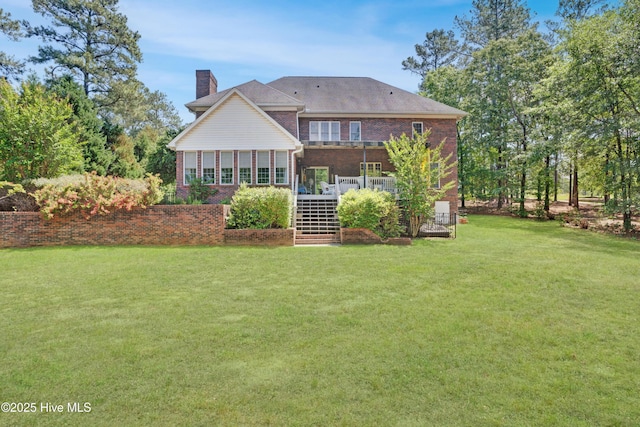 back of house featuring a yard, a chimney, a deck, stairway, and brick siding