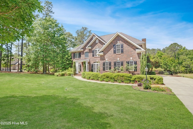 view of front of house with a chimney, a front yard, brick siding, and concrete driveway