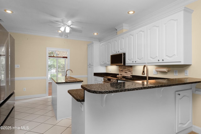 106 Oakmont Cir, New Bern, NC 28562 - kitchen with stainless steel microwave, a ceiling fan, a peninsula, an island with sink, and white cabinets