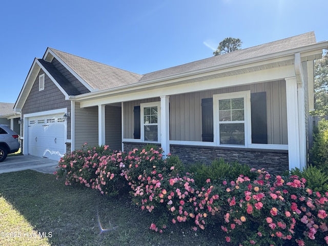 view of side of property featuring board and batten siding, an attached garage, concrete driveway, and a porch