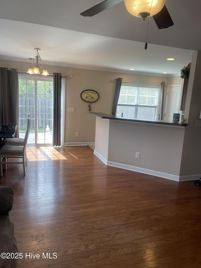 unfurnished living room featuring baseboards, dark wood-type flooring, crown molding, and ceiling fan with notable chandelier