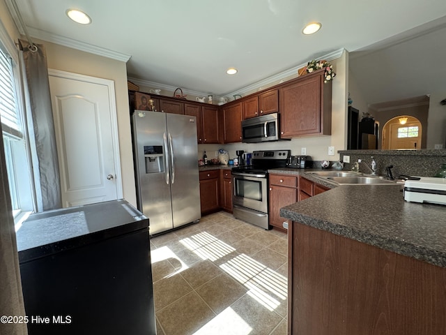 kitchen with light tile patterned flooring, dark countertops, appliances with stainless steel finishes, a sink, and ornamental molding