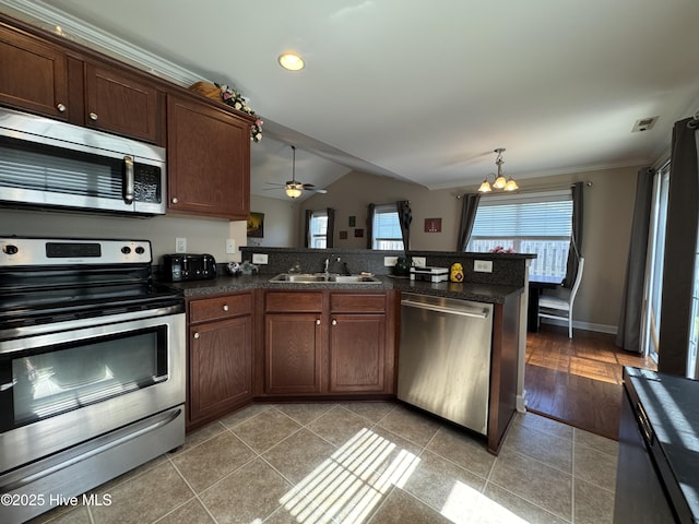kitchen featuring appliances with stainless steel finishes, dark countertops, a sink, a peninsula, and lofted ceiling