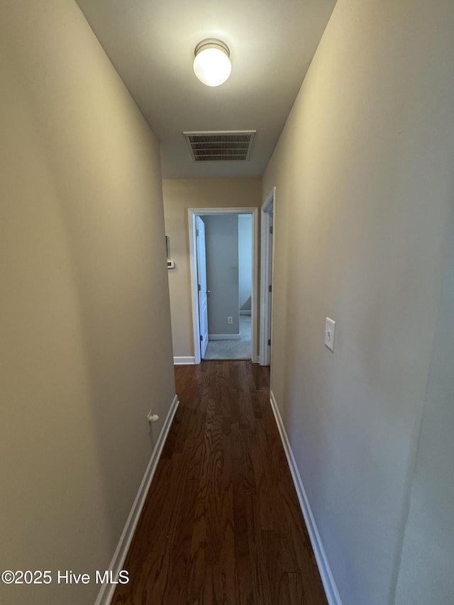 hall with visible vents, baseboards, and dark wood-style floors