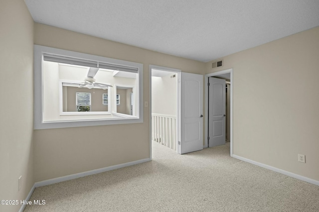 carpeted spare room featuring visible vents, baseboards, and ceiling fan
