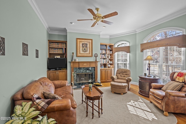 living room featuring light wood-style floors, a ceiling fan, crown molding, and a fireplace