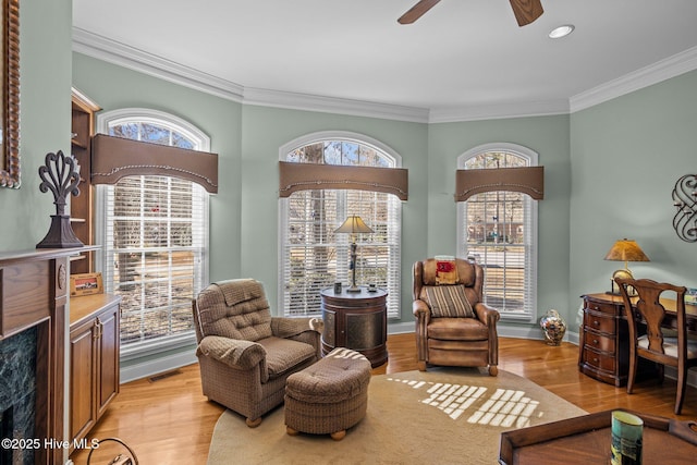 living area with a ceiling fan, baseboards, ornamental molding, and light wood-style floors