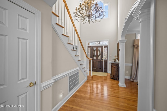 foyer entrance featuring stairs, baseboards, light wood-type flooring, a chandelier, and arched walkways