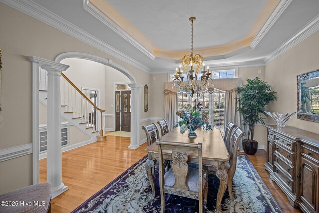 dining area with a notable chandelier, decorative columns, wood finished floors, and a tray ceiling